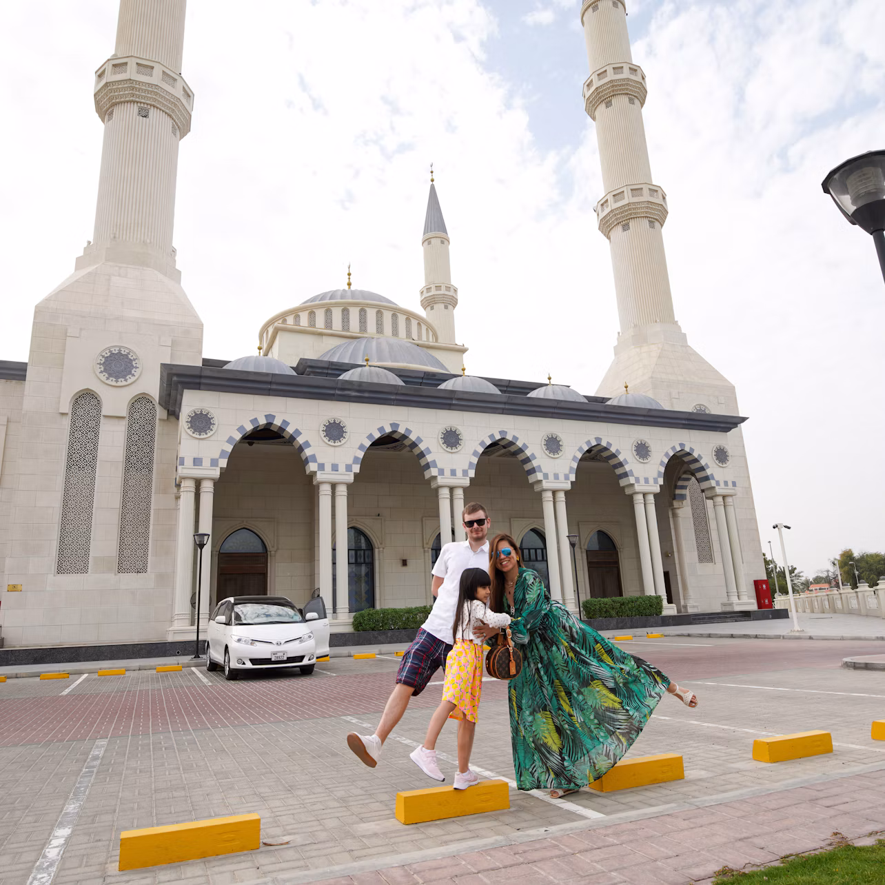 A family poses in front of a mosque with tall minarets on a partly cloudy day.