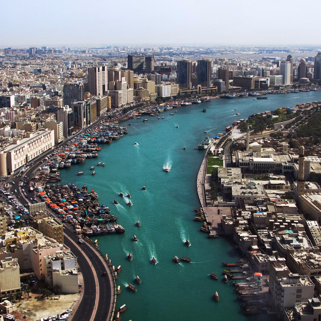 Aerial view of a cityscape with high-rise buildings, a river with boats, and densely packed structures on both banks.
