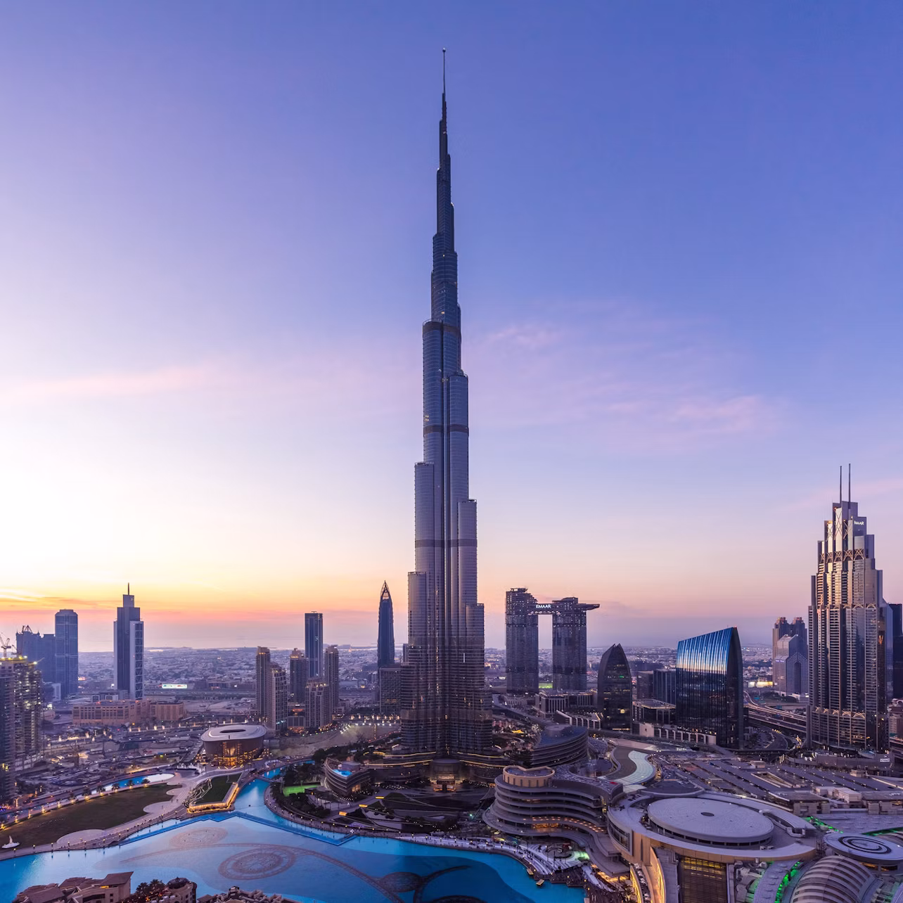 Skyline at sunset featuring a tall skyscraper with surrounding modern buildings and a winding water feature.