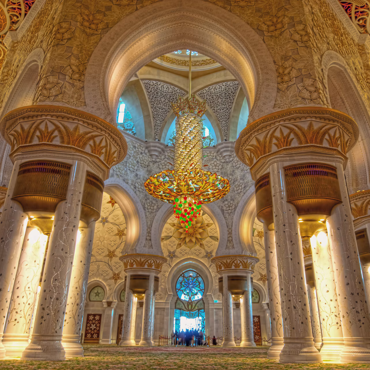Ornate interior of a mosque with intricate pillars, grand arches, and a large, colorful chandelier hanging from the ceiling.