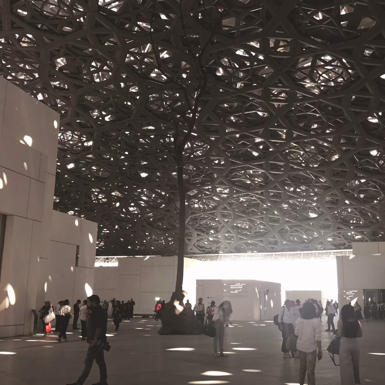 A modern indoor space with geometric ceiling patterns. People are gathered around under natural light.
