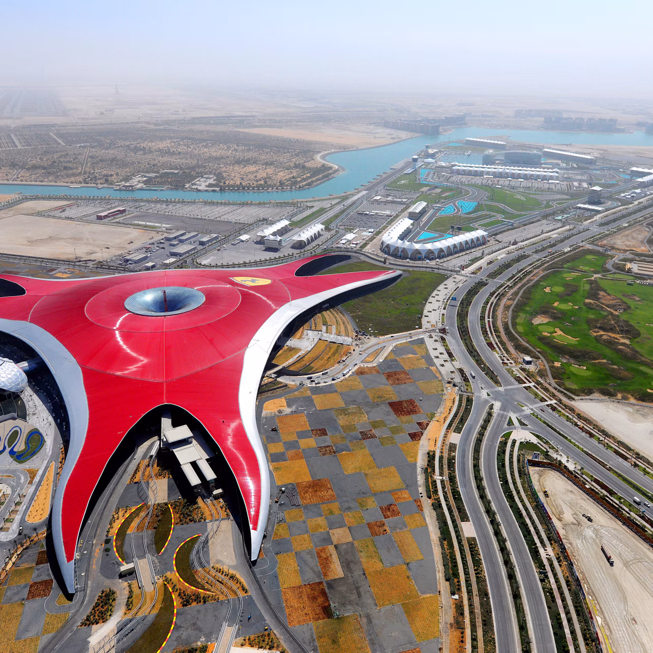 Aerial view of a large, red-roofed building shaped like a starfish, with surrounding roads, patches of greenery, and waterway.