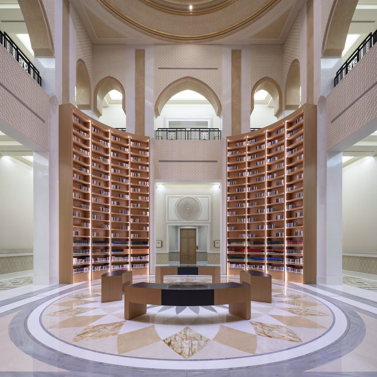 A grand library interior with high, arched ceilings, tall curved bookshelves, a circular desk, and ornate floor patterns.