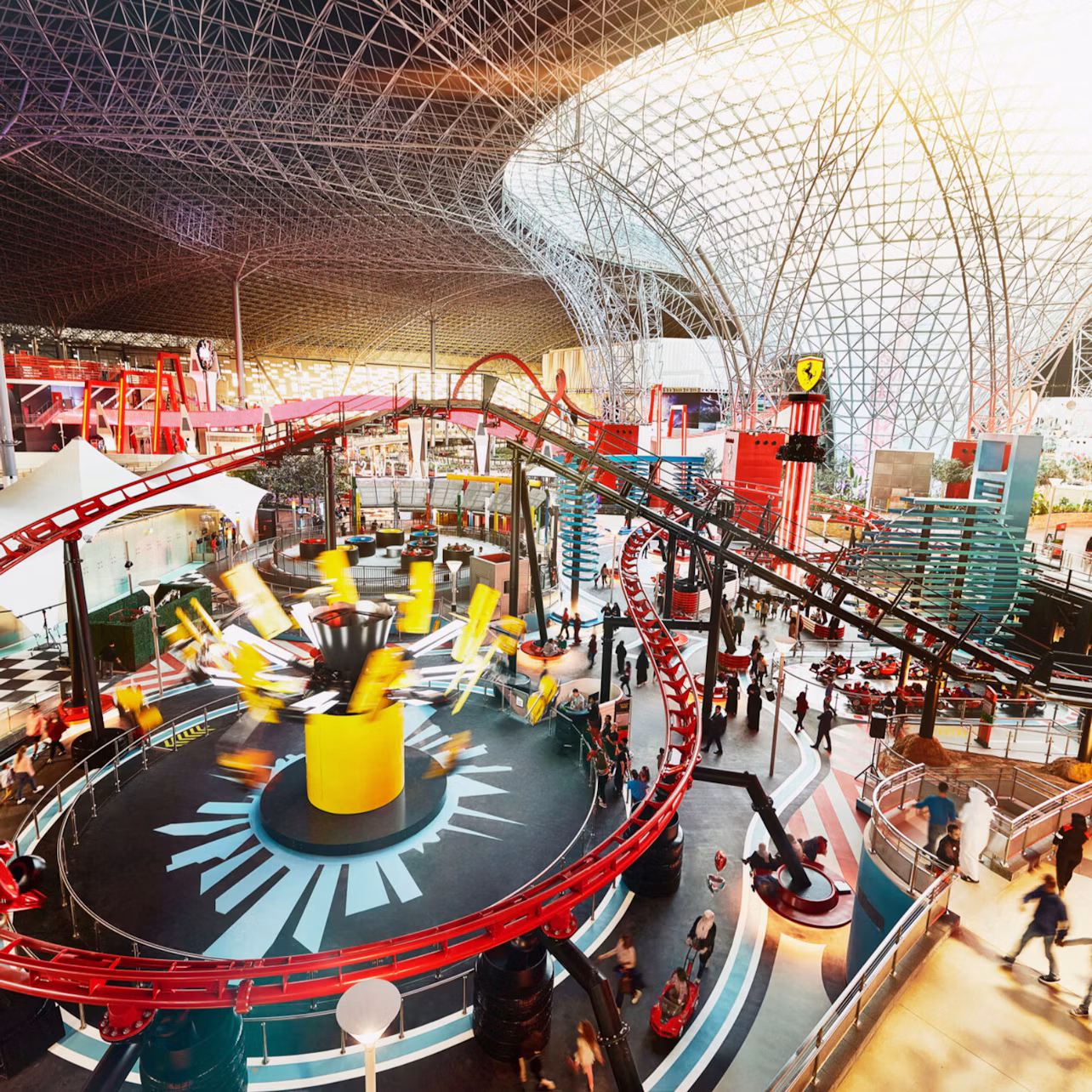 Indoor amusement park with a rollercoaster and spinning ride under a large glass and steel dome structure.