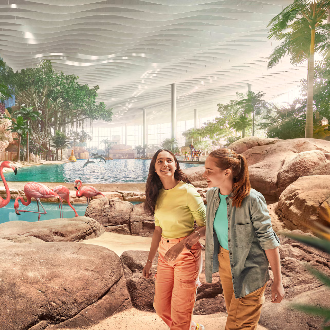 Two women walking in a tropical indoor setting with rocks, trees, and flamingos near a pool.