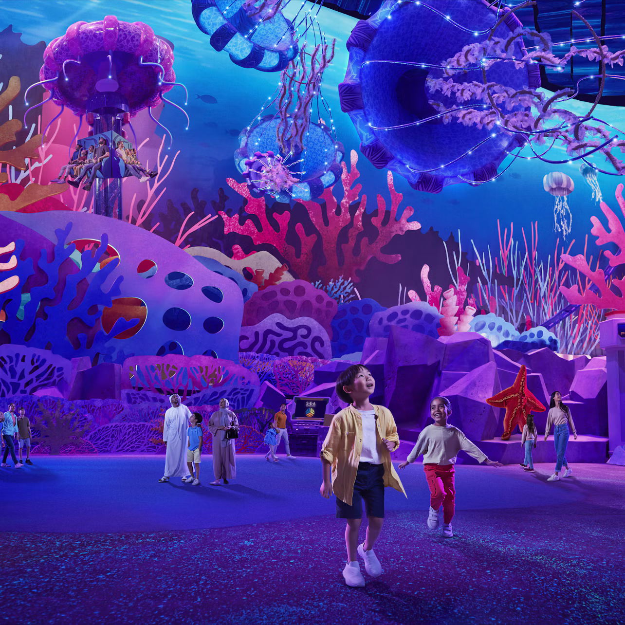 Children and adults exploring an underwater-themed exhibit with vibrant, colorful coral, jellyfish, and marine life decor.