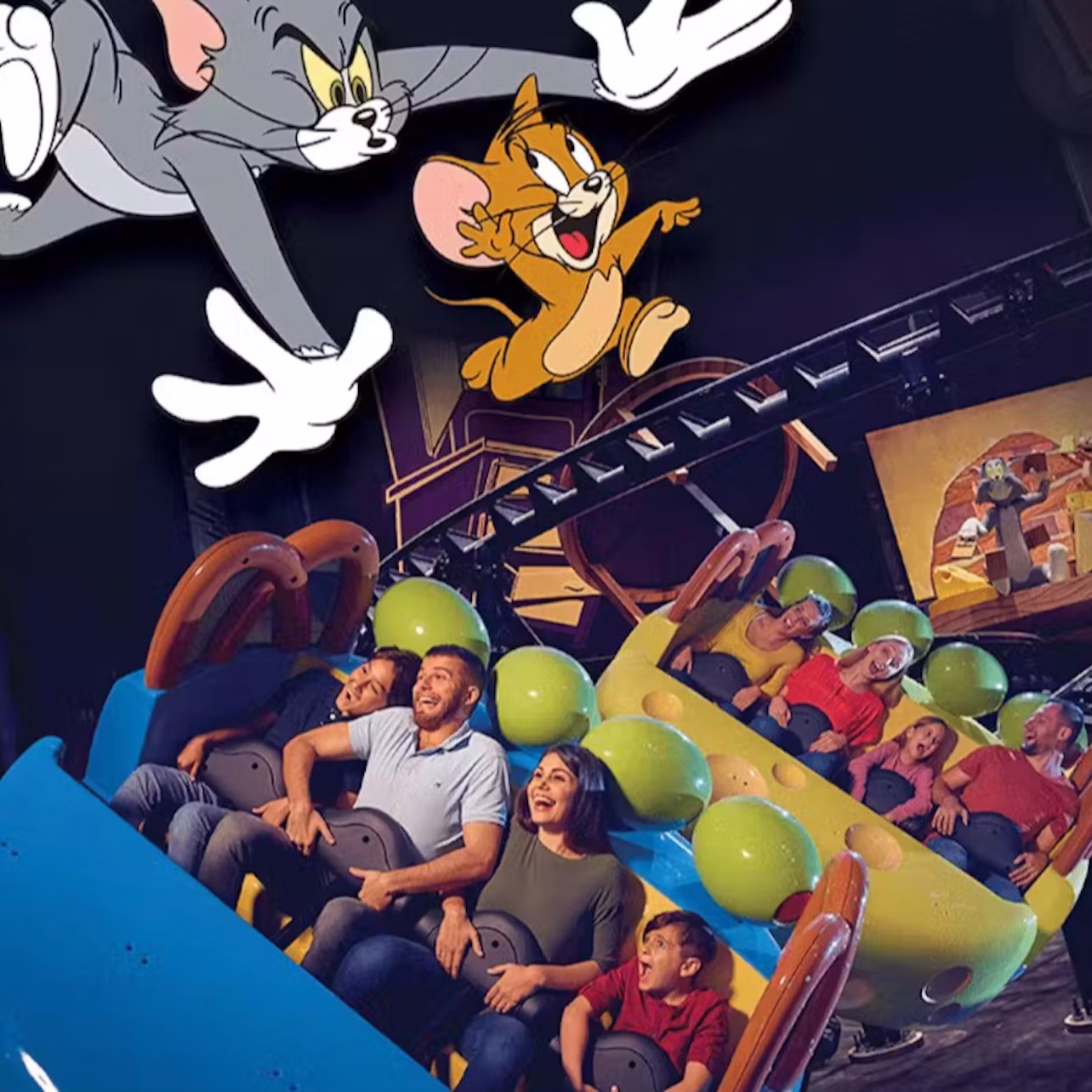 A group of people enjoying a colorful roller coaster ride indoors, with Tom and Jerry characters depicted above them.