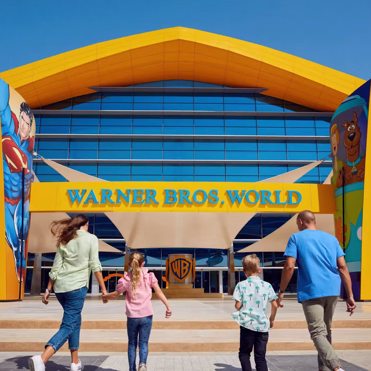 A family walking towards the entrance of Warner Bros. World theme park, featuring superhero and cartoon character decorations.