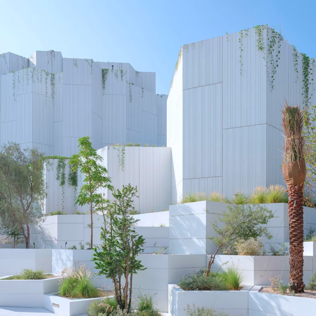 White modern buildings with cascading greenery and a landscaped garden featuring various plants and trees in the foreground.