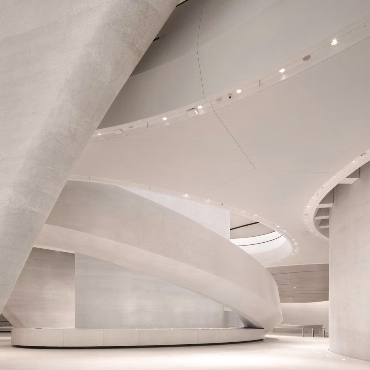 A modern interior featuring curved architectural elements, smooth white surfaces, and soft lighting.