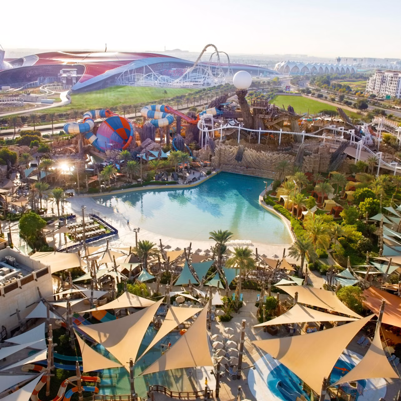 A large outdoor water park with pools, slides, and attractions, surrounded by greenery and structures under a sunny sky.