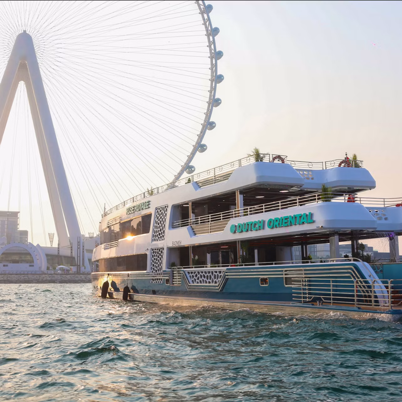A large double-deck boat labeled "Dutch Oriental" on water near a ferris wheel at sunset.