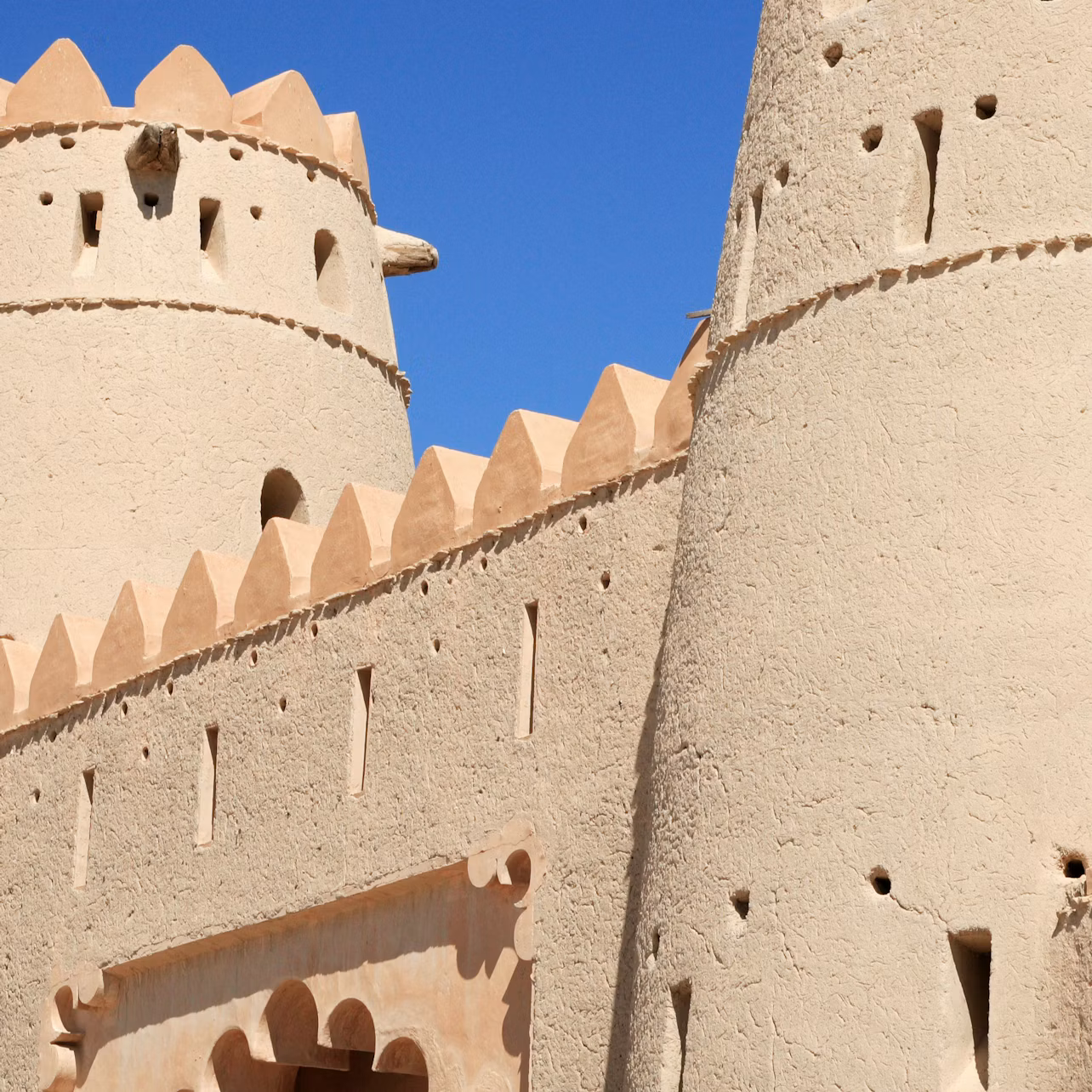 Close-up of an adobe fort with towers and decorative crenellations under a clear blue sky.
